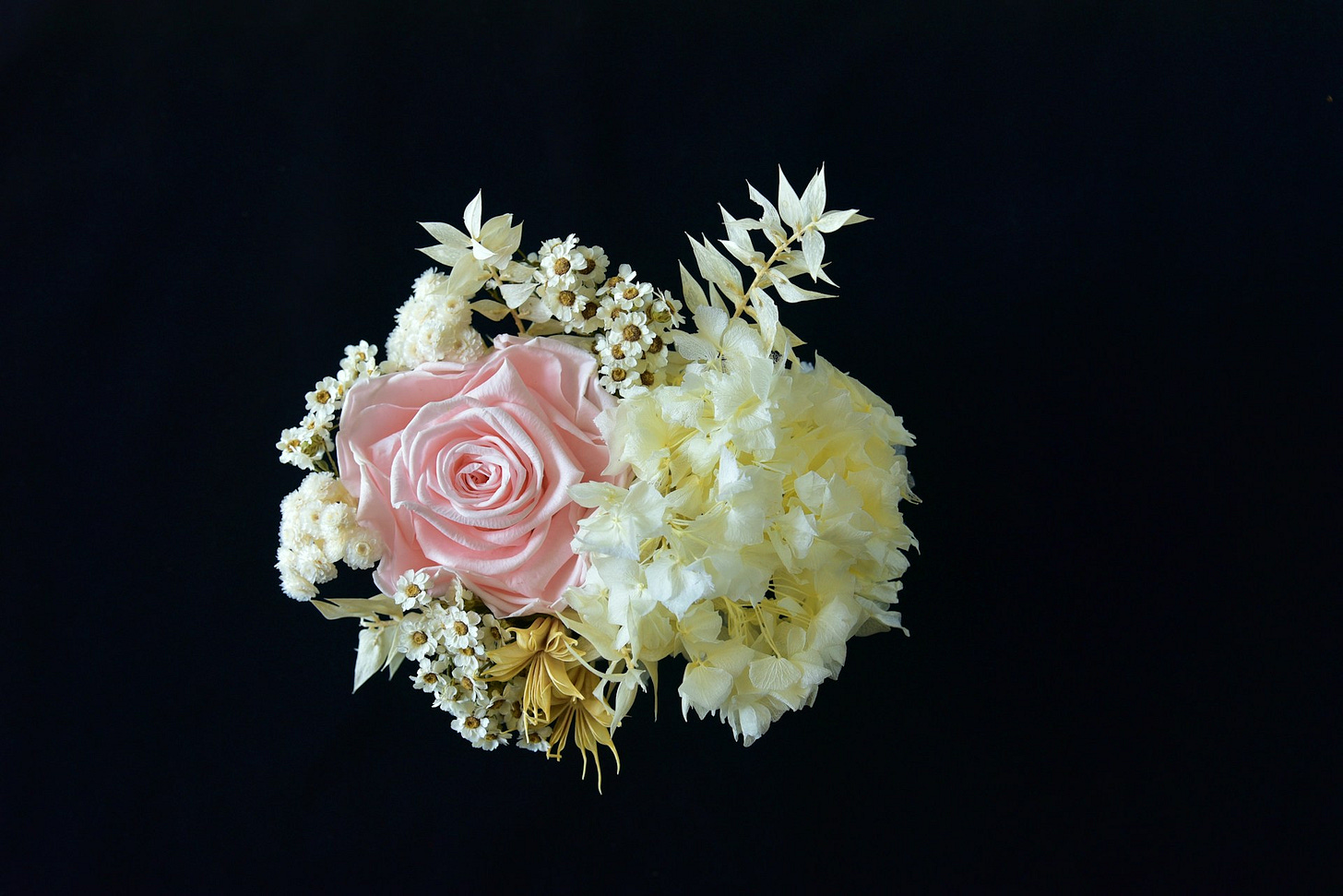 A delicate floral arrangement featuring a soft pink rose, pale hydrangeas and small white blossoms against a black background. Photo by Arturo Alvarez on Unsplash