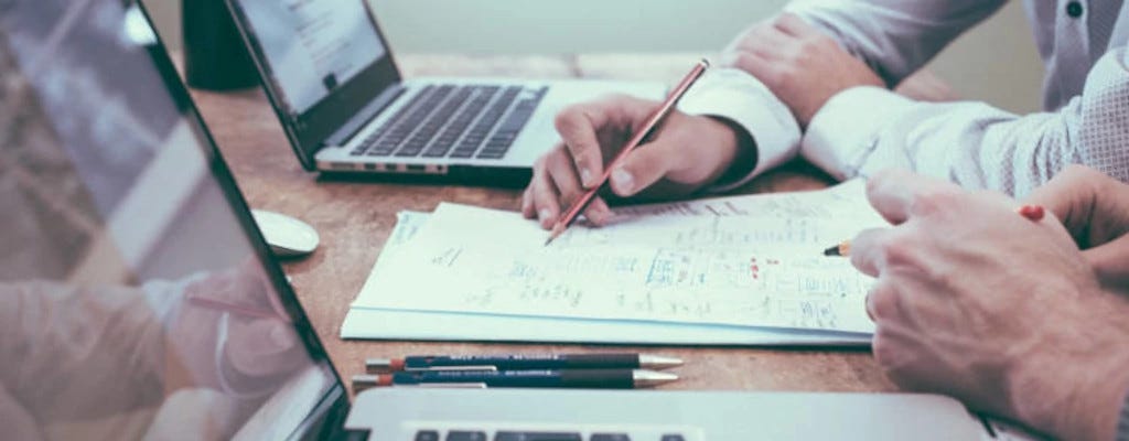 Stock photo of two people having a conversation and writing on a paper in front of two open laptops.