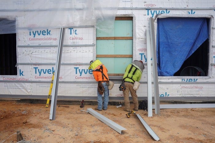 Two construction workers in safety gear work on a building