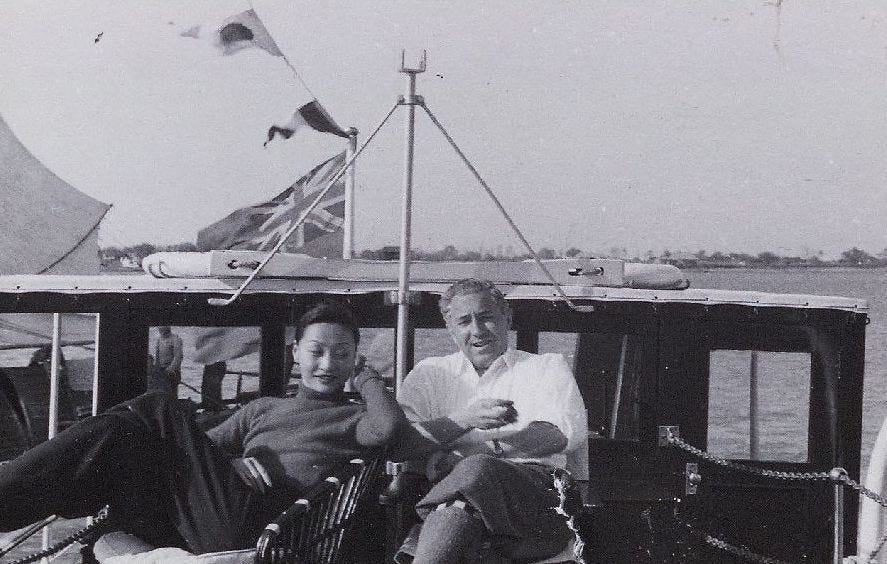 Anna May Wong sits next Chester Fritz on a sail boat with the wind blowing the flags in the background Anna May Wong sits next Chester Fritz on a sail boat with the wind blowing the flags in the background