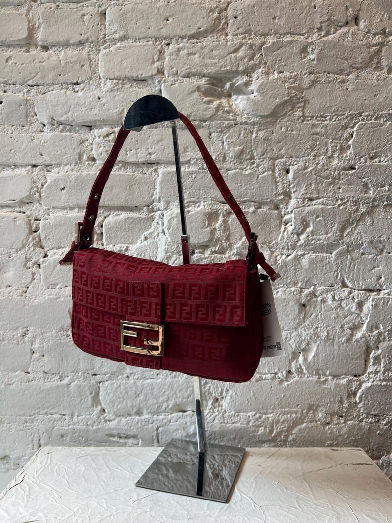 May include: A red quilted shoulder bag with a gold Fendi logo. The bag is on a silver stand.