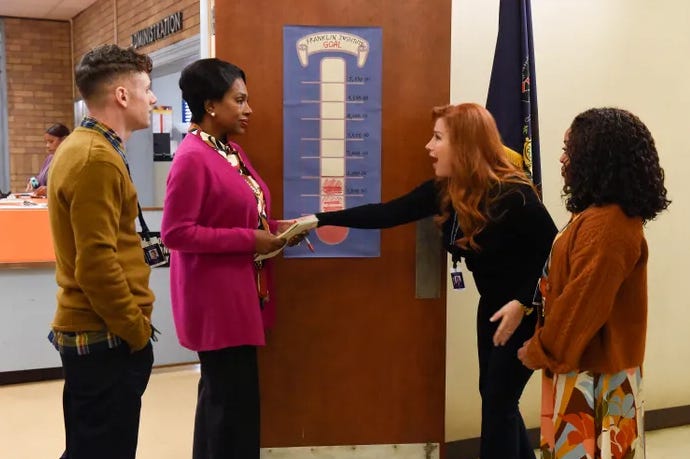 Four people stand near a fundraiser tracking poster.