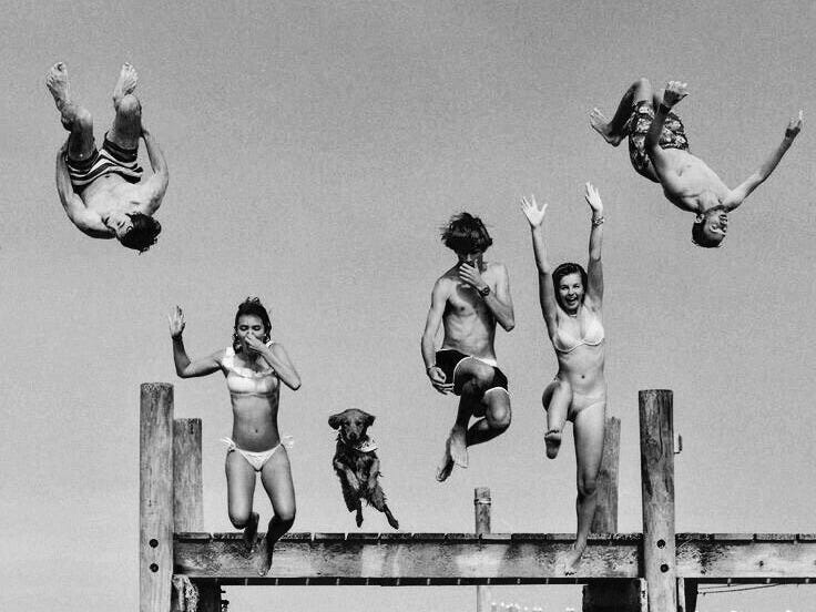 This may contain: four people jumping off a pier into the water