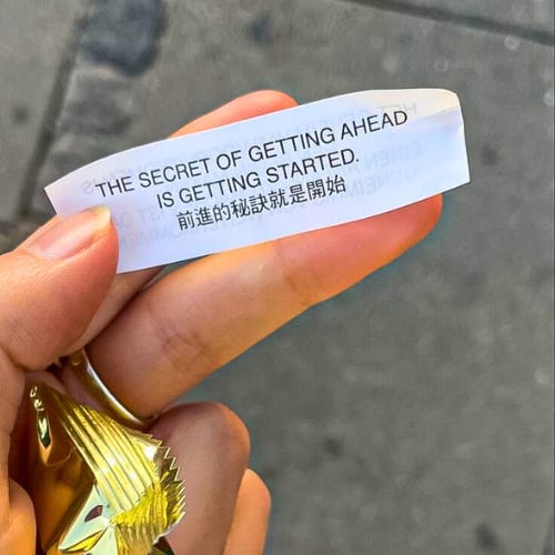 Someone holding a fortune cookie paper that reads, “The secret to getting ahead is getting started.”