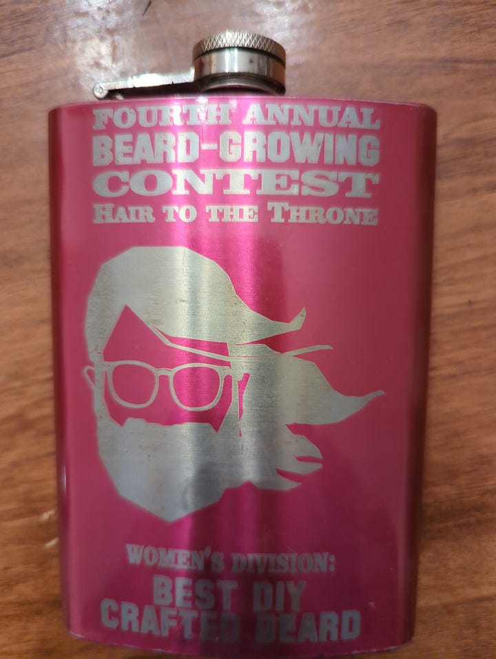 Left: me in a straw farmer hat, plaid shirt and overalls, wearing a sprouted beard. Right: pink flask with bearded lady engraved on it.