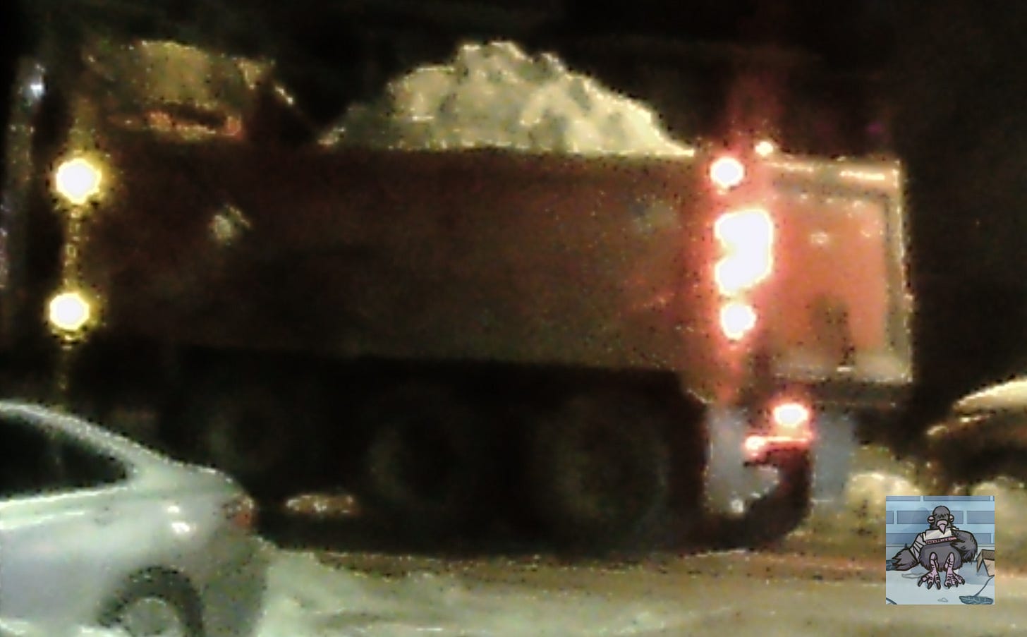 A dumptruck is filled with snow on a city street at night.