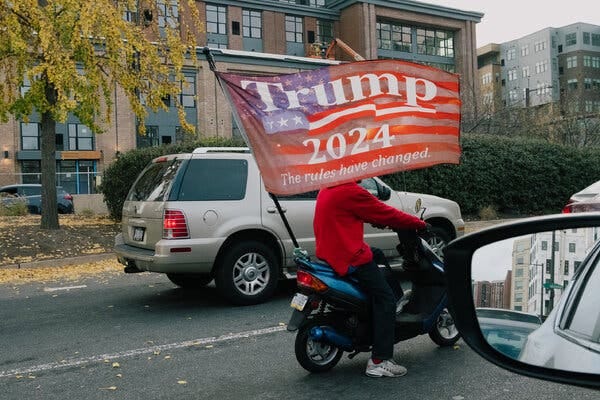 A person riding a moped with a Trump 2024 flag on a street.