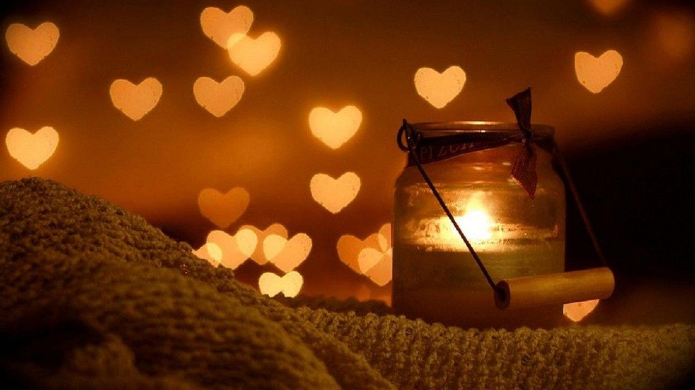 A glowing candle inside a jar casts warm light with heart-shaped bokeh, capturing love and cozy photography vibes.