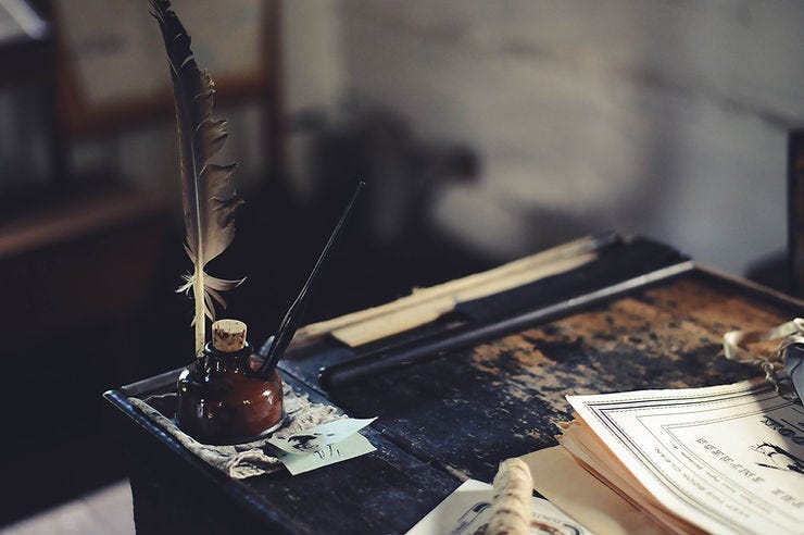 A feather ink pen sitting on an old desk. A feather ink pen sitting on an old desk.