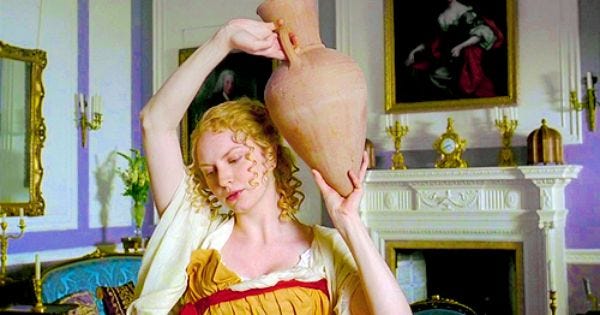 Harriet Smith is posing in Grecian dress, holding a vase above her head. 