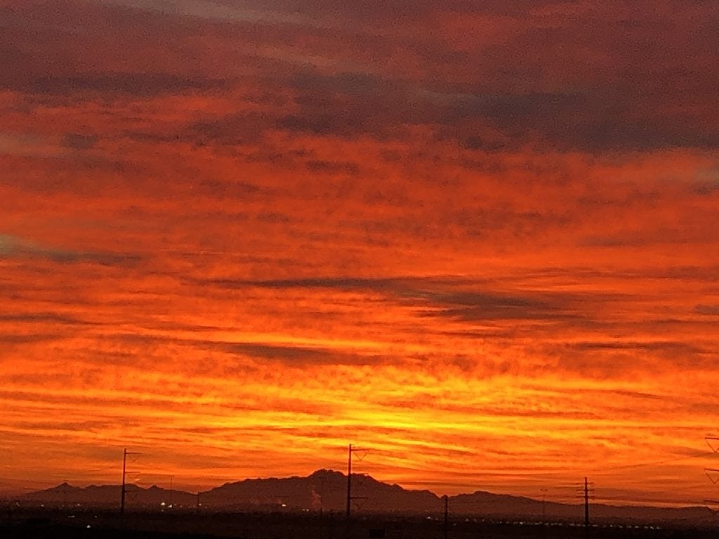a sky at sunset with hot oranges, red, and blacks intermixed in the sky hovering over a distant, dark mountain. a sky at sunset with hot oranges, red, and blacks intermixed in the sky hovering over a distant, dark mountain.