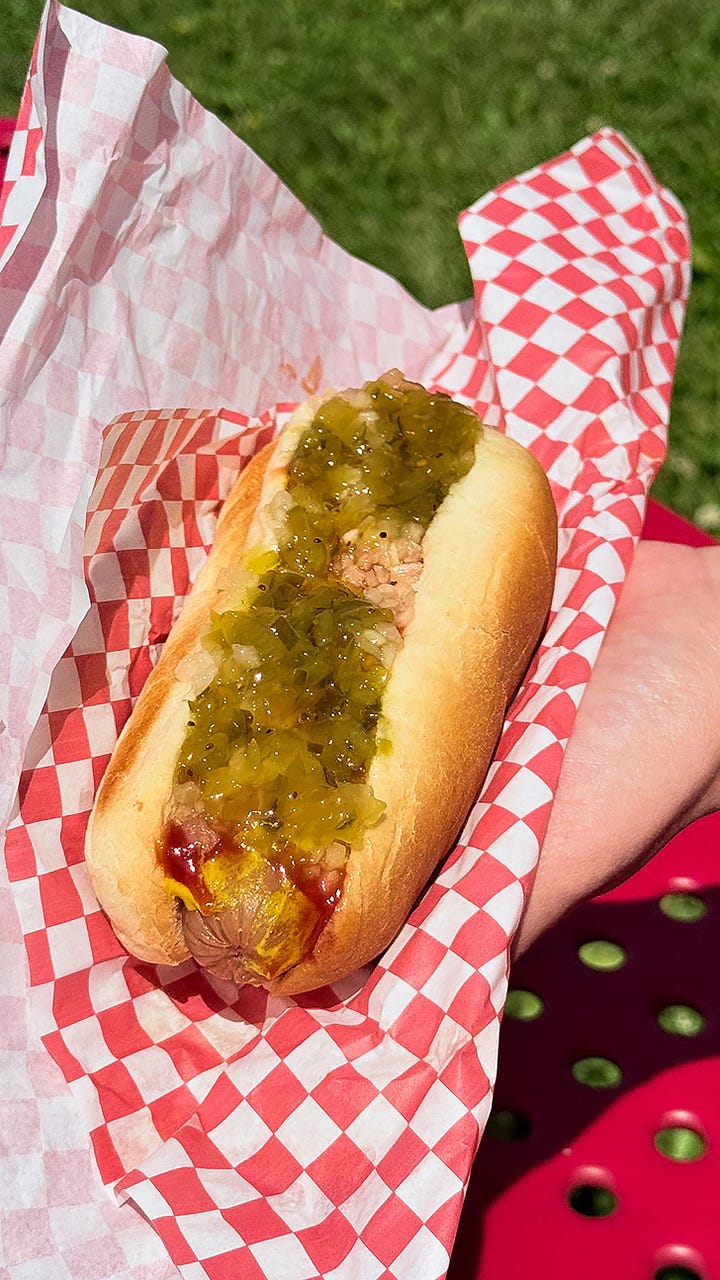 3 burgers with meet and sauces covering the red and white checkered wrappers. Close up of the SPAM dog with relish, onions, ketchup and mustard.