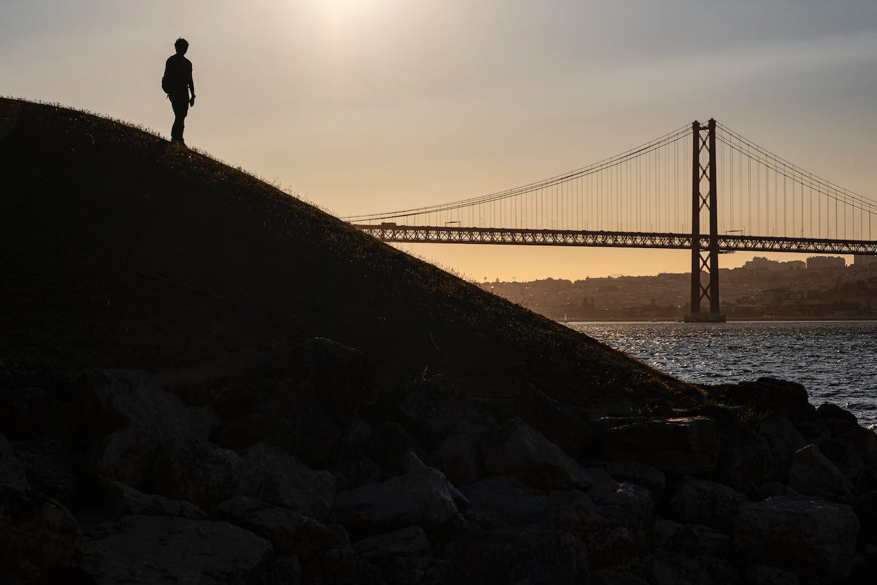 a silhouette of a person walking with the 25 de Abril bridge over the river Tejo in the background