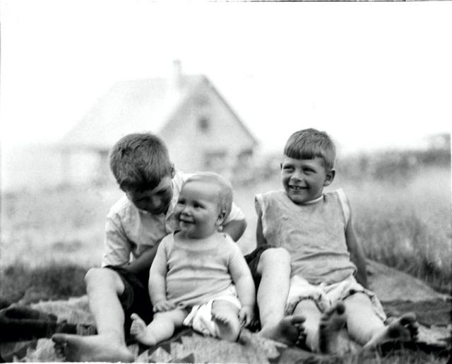 James Howard as a baby in a wooden box on the porch of the Howard cottage; Brooks and Frank with the infant Jimma, the Howard cottage in the background
