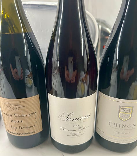 bottles of French wine from two tastings. Wines of Burgundy and the Loire Valley. Plates of appetizers on a wooden table.