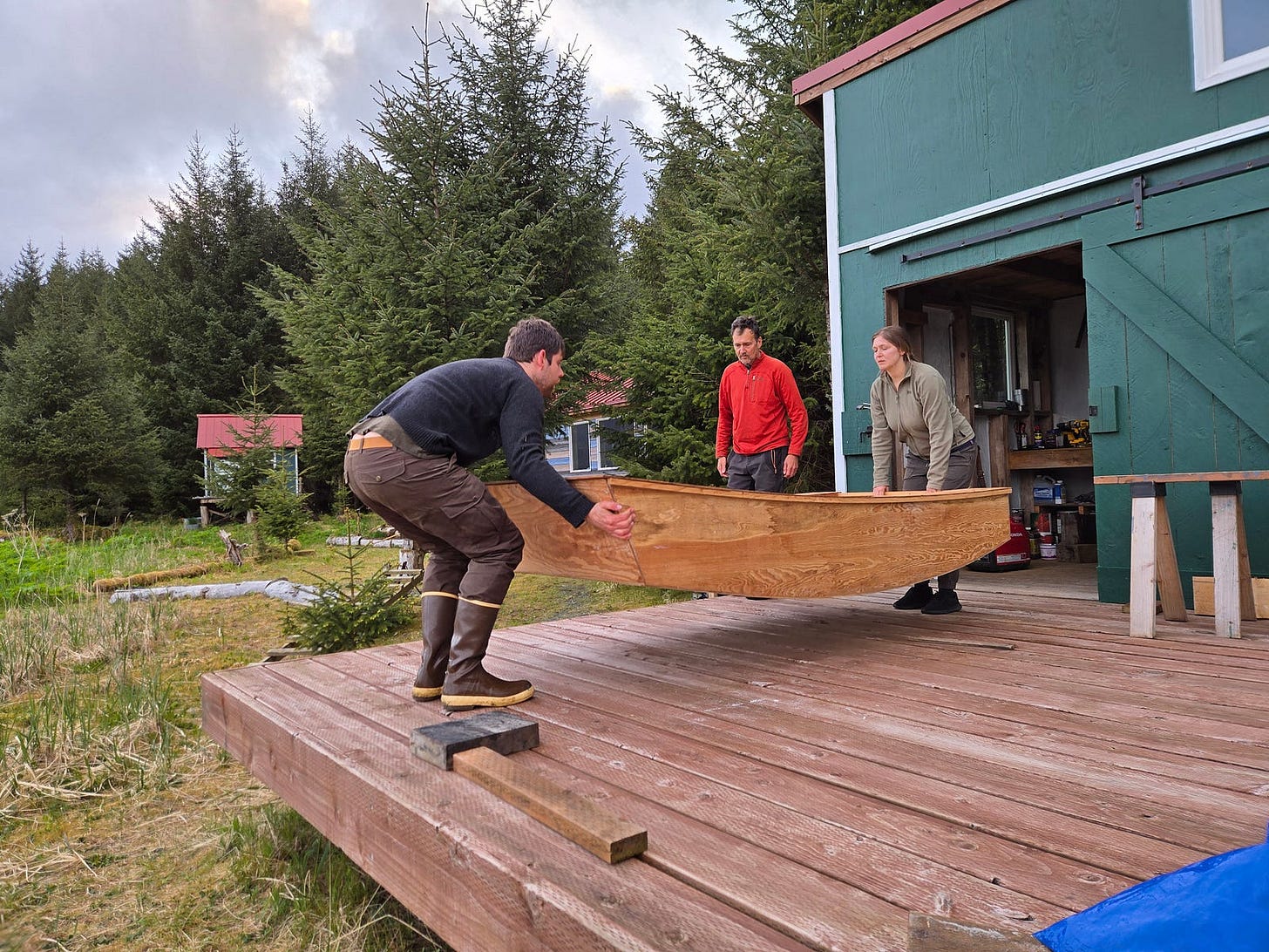 A man and woman (Robert and Kelsey) lifting a boat hull, with a man in the background