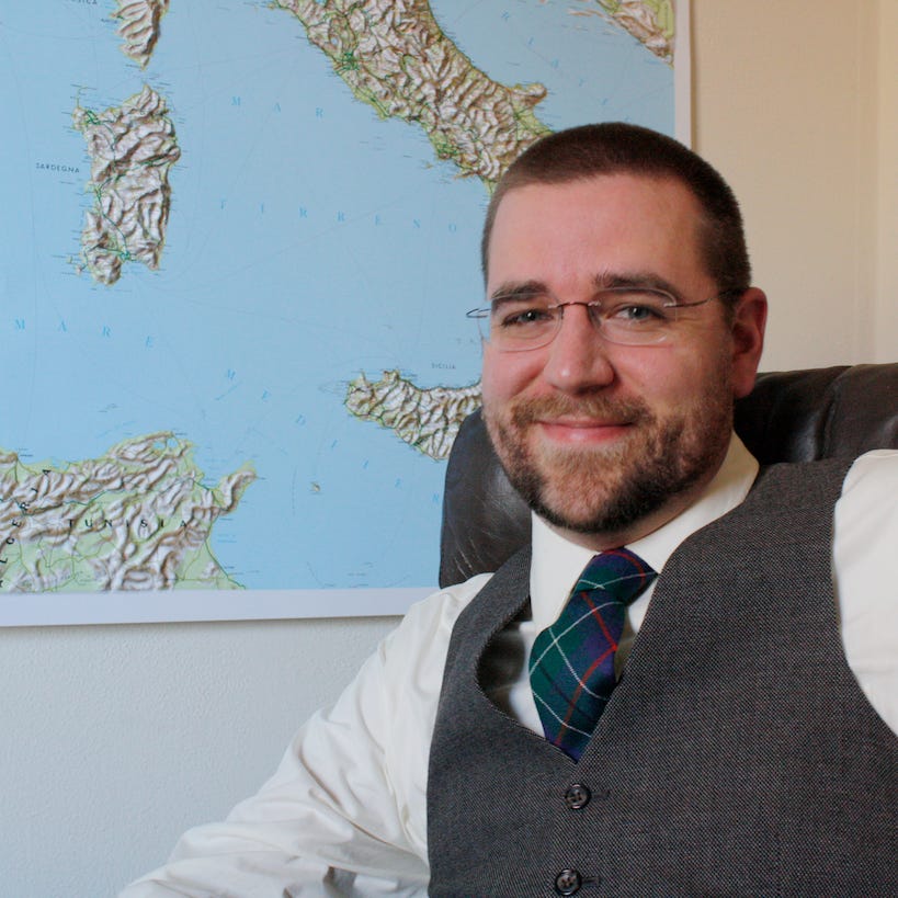 A man in glasses, wearing a vest and tie, sits before a map of Italy on the wall, lost in thought as if planning a Martian Revolution. A man in glasses, wearing a vest and tie, sits before a map of Italy on the wall, lost in thought as if planning a Martian Revolution.