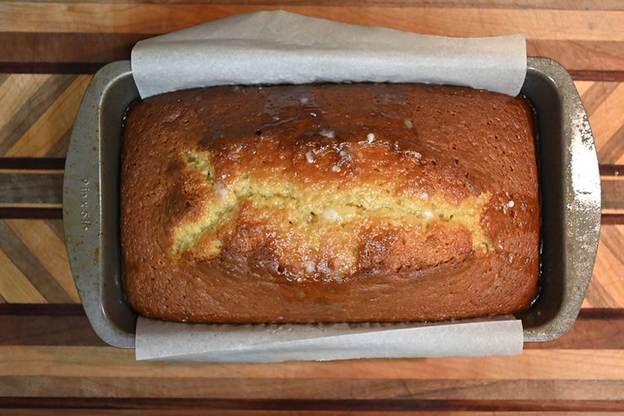 Golden brown loaf cake in a metal pan lined with parchment paper, on a wooden board with geometric patterns. Golden brown loaf cake in a metal pan lined with parchment paper, on a wooden board with geometric patterns.