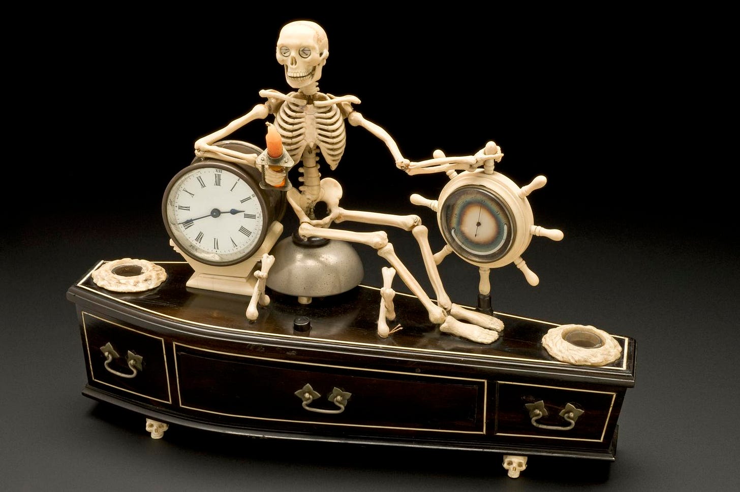 A model of a smiling skeleton sitting on a clock above a coffin