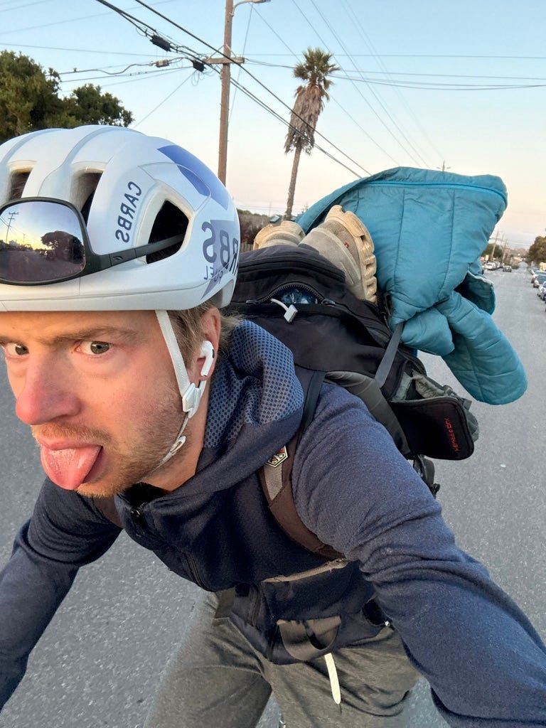 person looking tired riding a bike up a hill with a backpack on