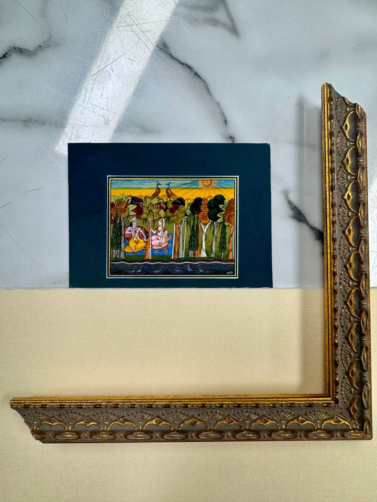 Small miniature painting resting on a large ornate gold frame corner against a marble surface.