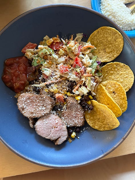 a blue bowl pictured with 3 different foods: salad, hummus, and pork tenderloin