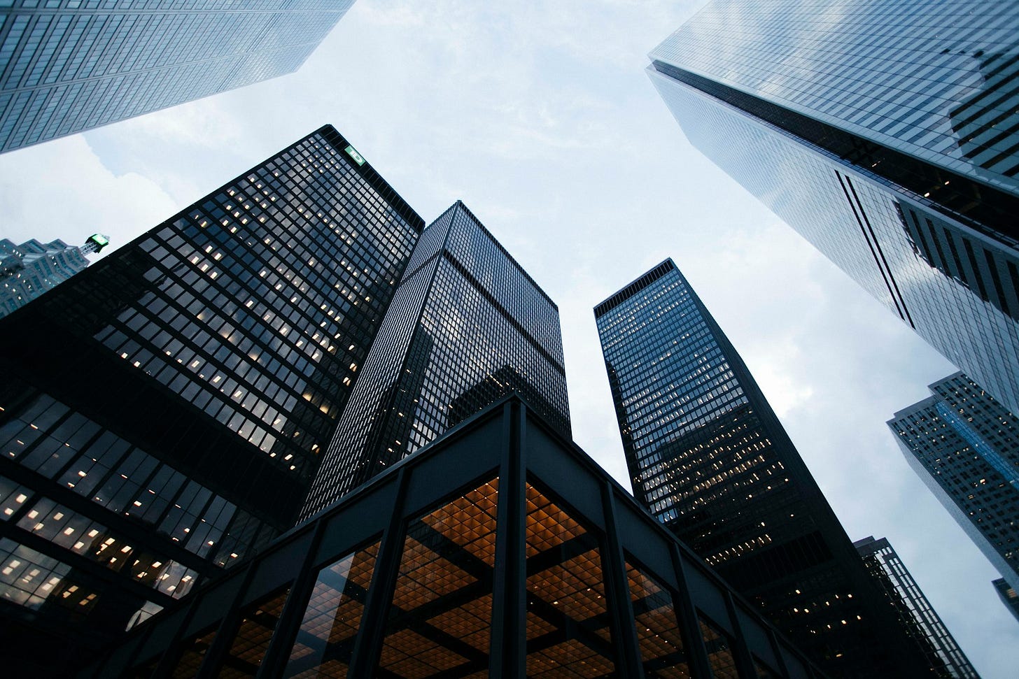 Upward view of tall glass skyscrapers with office lights on against a cloudy sky. Upward view of tall glass skyscrapers with office lights on against a cloudy sky.