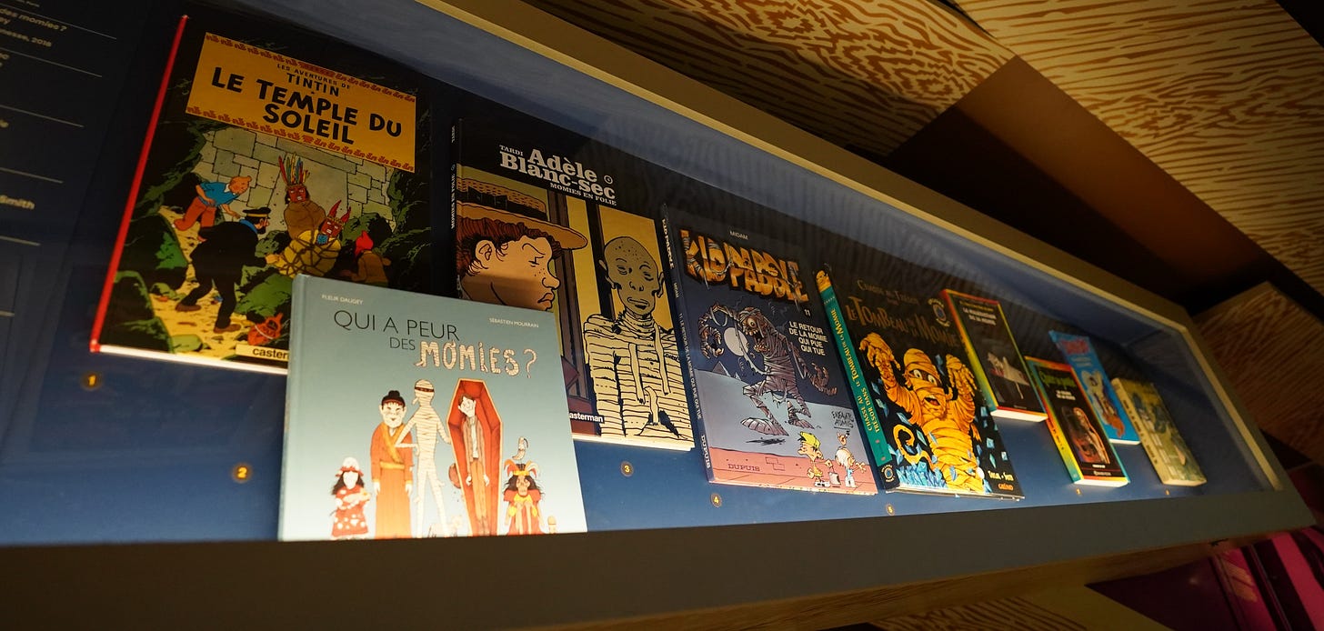 A display case in the Paris Momies exhibition containing mummy-themed comic books and illustrated children’s books.
