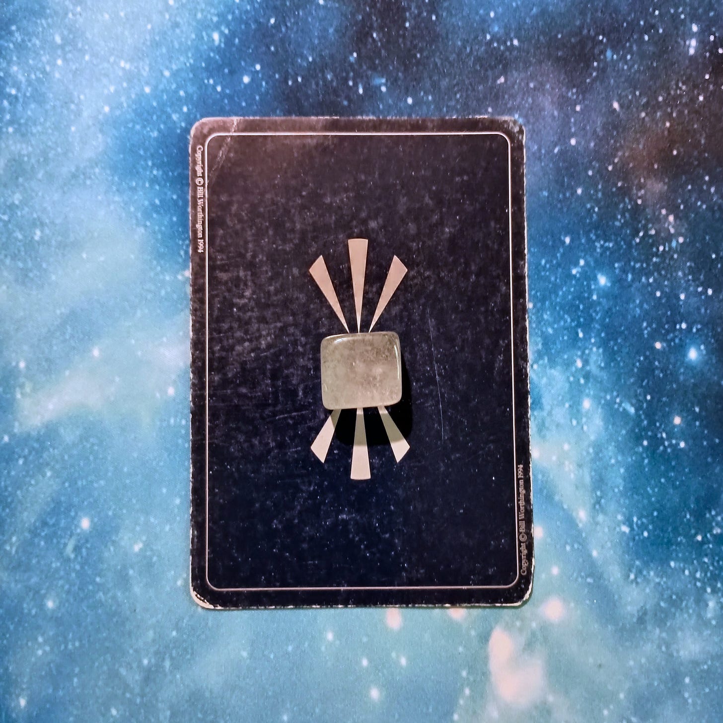 New Moon Magic: Your July 2025 Pick-a-Card Tarot Reading, pile 1 - clear quartz stone and an oracle card, face down, on a starry blue background