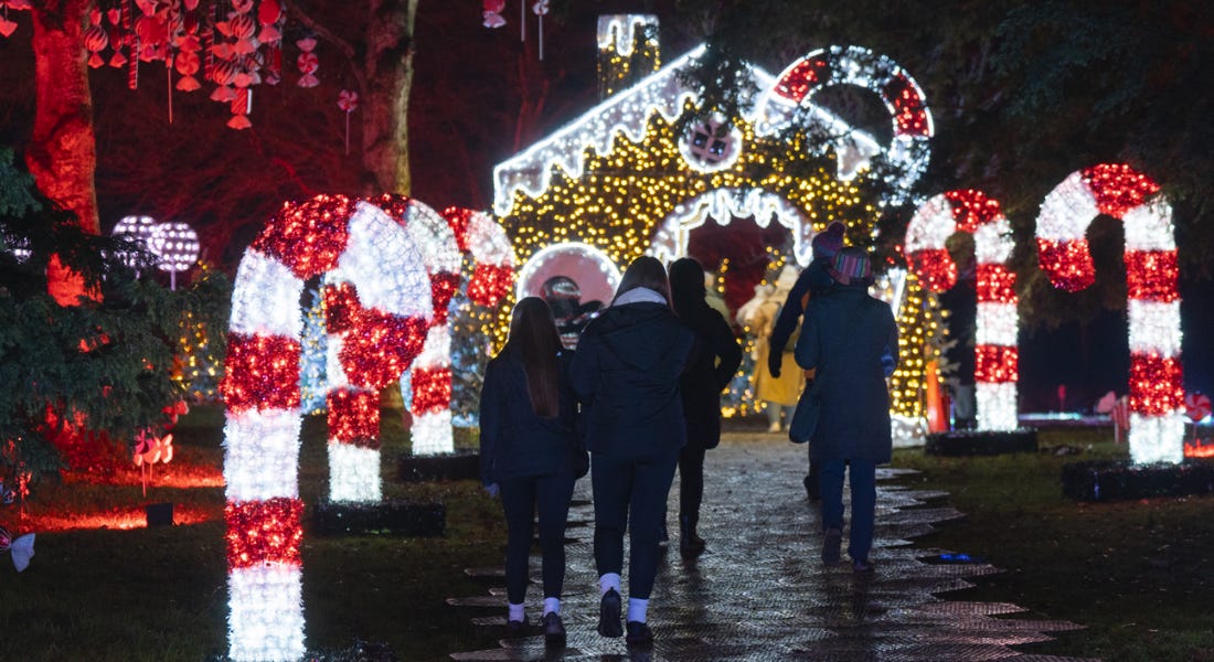 A Christmas light trail with light-up candy canes and a gingerbread house, with people walking on the path A Christmas light trail with light-up candy canes and a gingerbread house, with people walking on the path