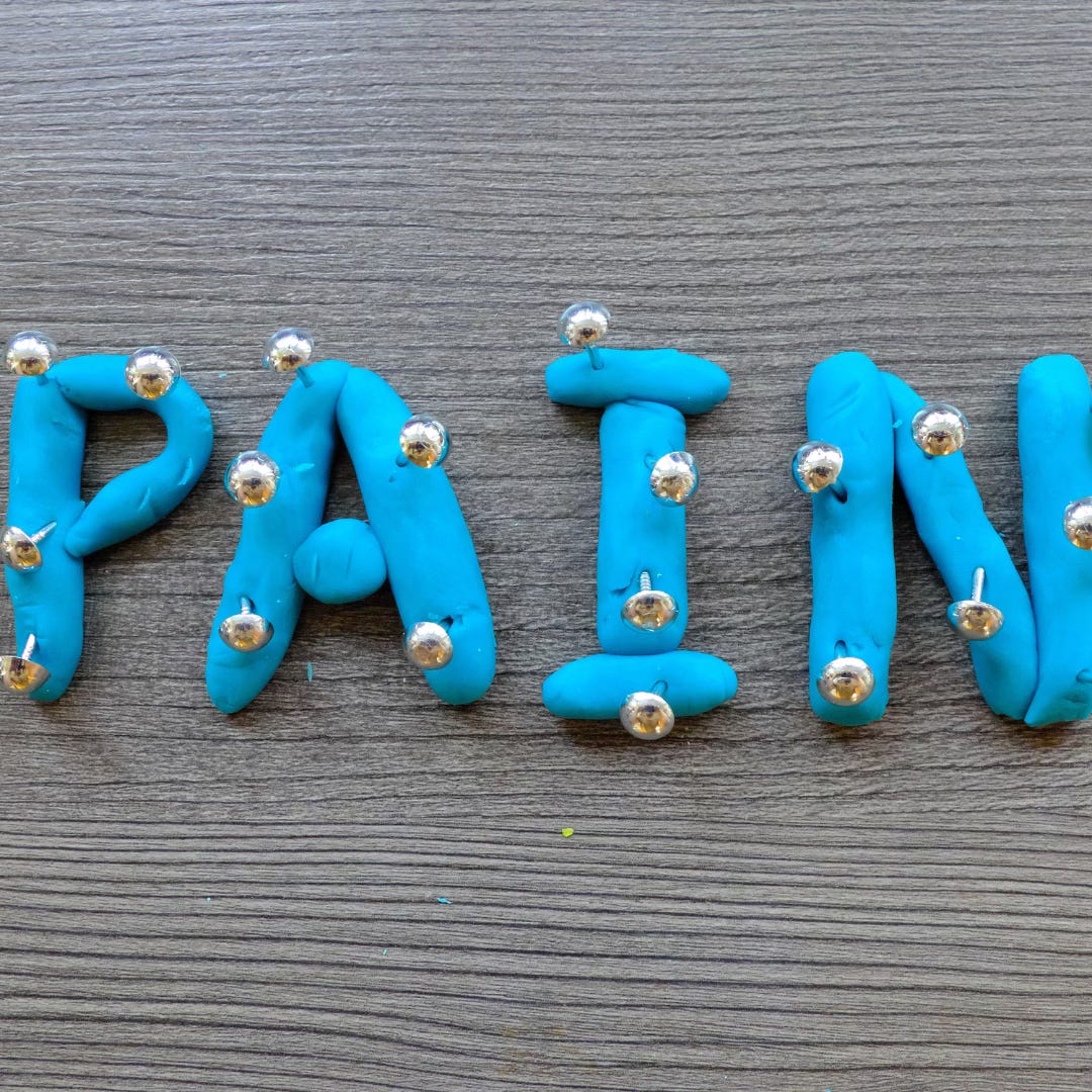 The word 'Pain' spelled out with blue clay and with needles sticking in the letters