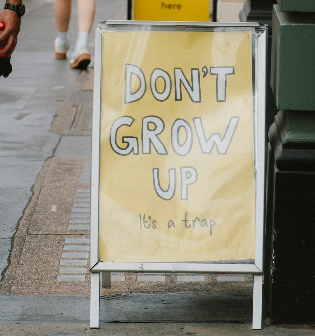 A-frame sign says "don't grow up, it's a trap."