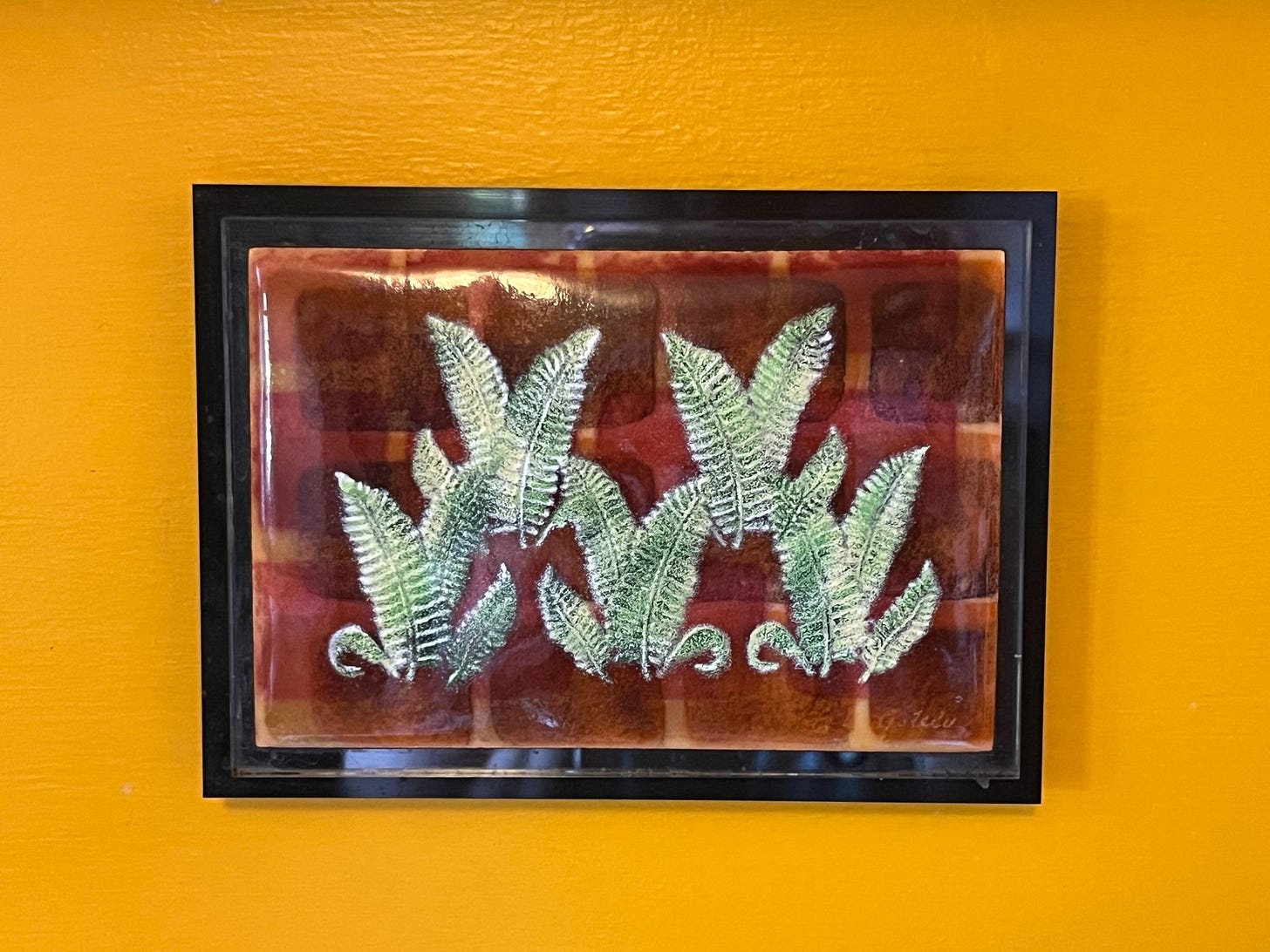Photo of piece of enameled art depicting ferns on a background of various color rectangles.