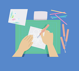 A person drawing on a piece of paper which has drawings and pencils around the table