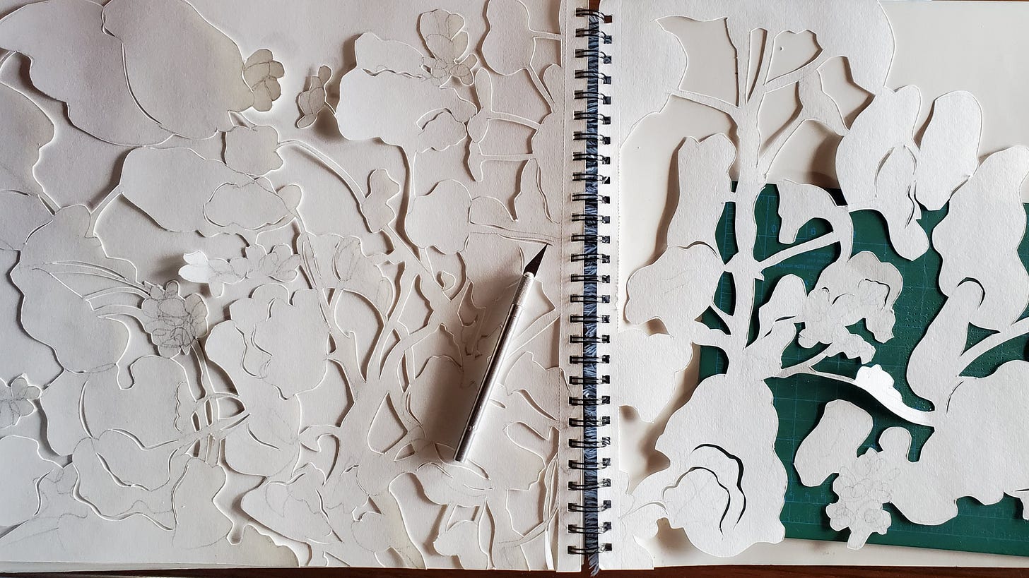 Image is of two large, white pieces of paper in a spiral-bound sketchbook. The book is opened flat, so that each page lies open and flat. Each page is cut out into the intricate shapes of a geranium plant with lots of stems and some flowers. Behind the cutout paper pages are more white pages of the sketchook. Underneath the righthand page cutout is a green cutting mat. On top of the lefthand page cutout is an exacto knife.