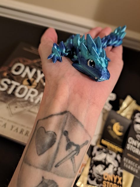 black sweater embroidered with Fourth Wing title and dragon, book, stickers, and signed bookplate for Onyx Storm by Rebecca Yarros