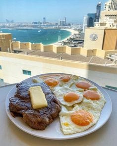 This may contain: a plate with eggs, meat and cheese on it next to a view of the ocean