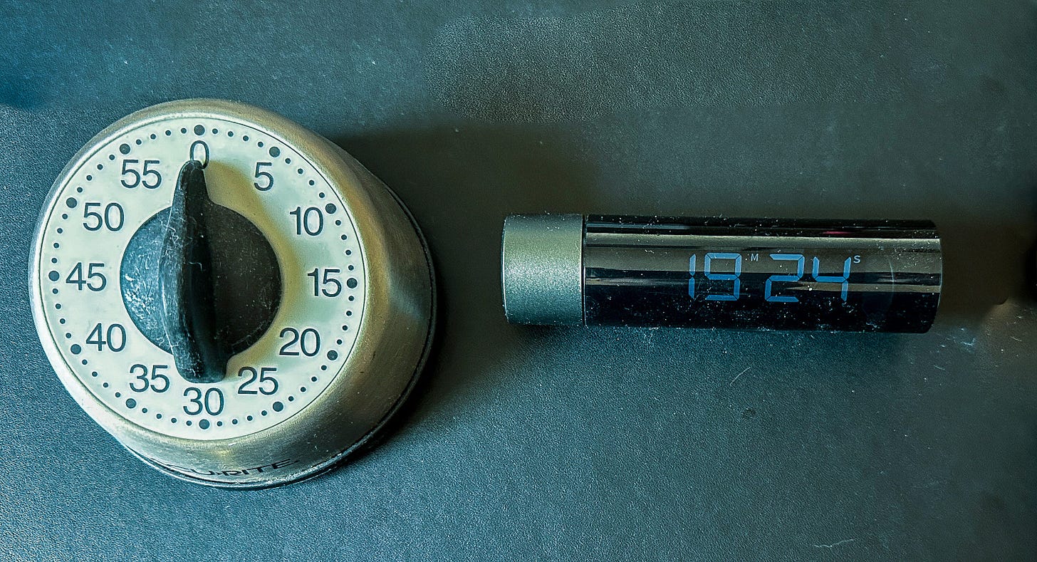 A rotary dial timer next to a cylindrical digital timer on a leather desk pad.