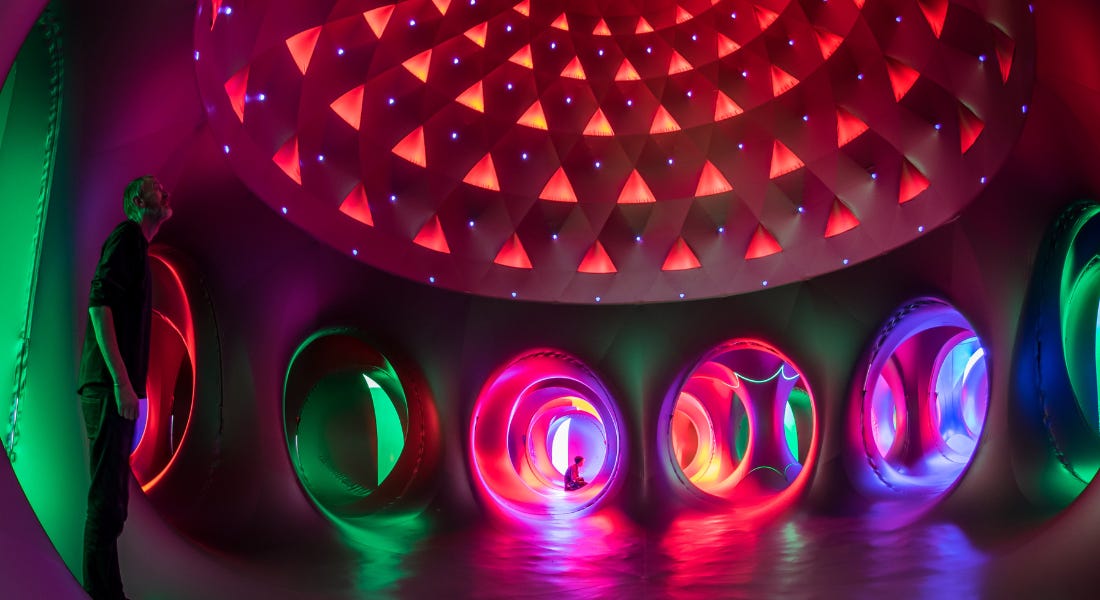 A colourful inflatable structure with green, pink, and red pods and a geometric ceiling