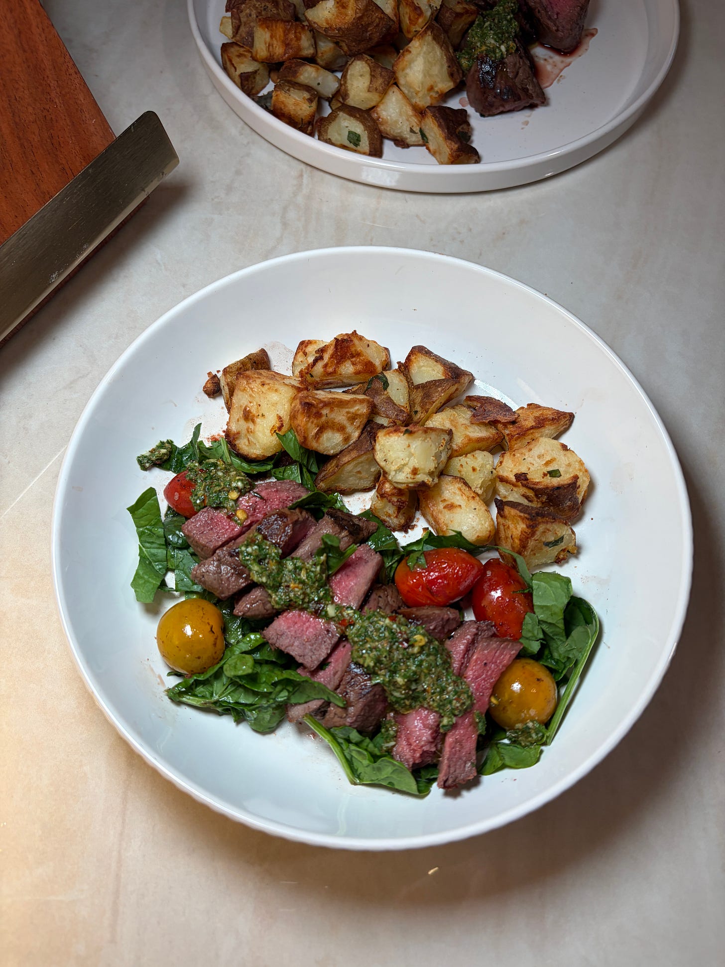chimichurri steak bowl with roasted potatoes and tomatoes on a bed of spinach