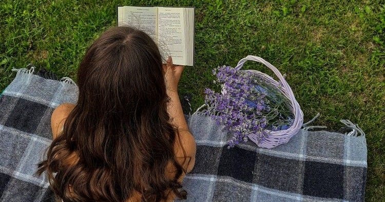 Girl reading among spring flowers and greenery, symbolizing the importance of taking a break from content creation