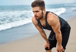 Man bent over with hands on knees after running on beach.