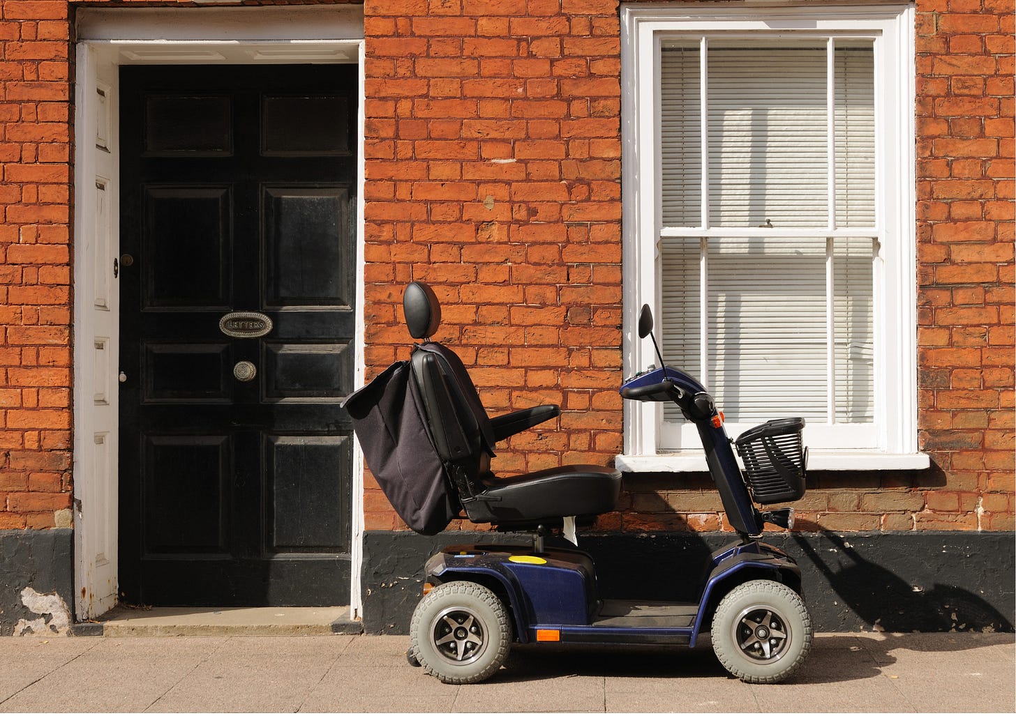 A large black and blue scooter with four wheels sitting in front of a red brick building