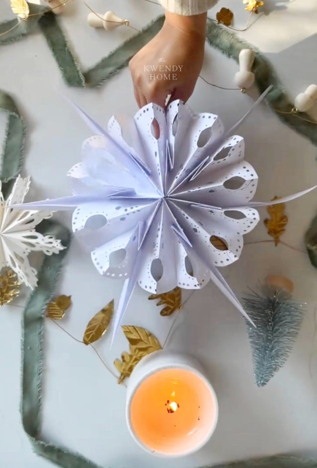 A series of photos taken from above a crafty work space where some of the steps are shown such as gluing paper bags together in layers, cutting patterned edges and using your hands to open up the sections. The space is decorated in small, varied Christmas related decor and craft supplies.