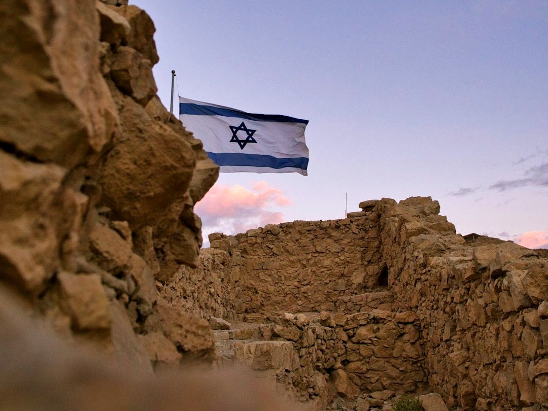 an israeli flag flying over a rocky area an israeli flag flying over a rocky area