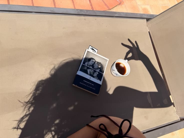 This may contain: a woman sitting at a table with a cup of coffee next to her shadow on the ground This may contain: a woman sitting at a table with a cup of coffee next to her shadow on the ground