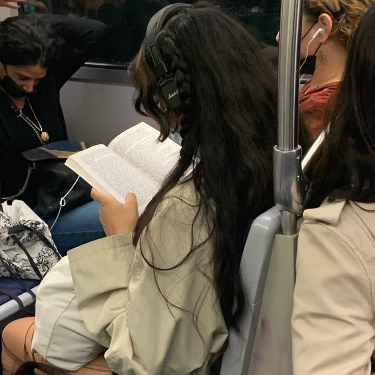 This may contain: some people sitting on a train and one is reading a book