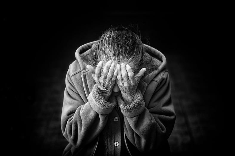 A black and white photo of an elderly woman wearing a winter coat and her head is bowed down and buried in her hands. A black and white photo of an elderly woman wearing a winter coat and her head is bowed down and buried in her hands.