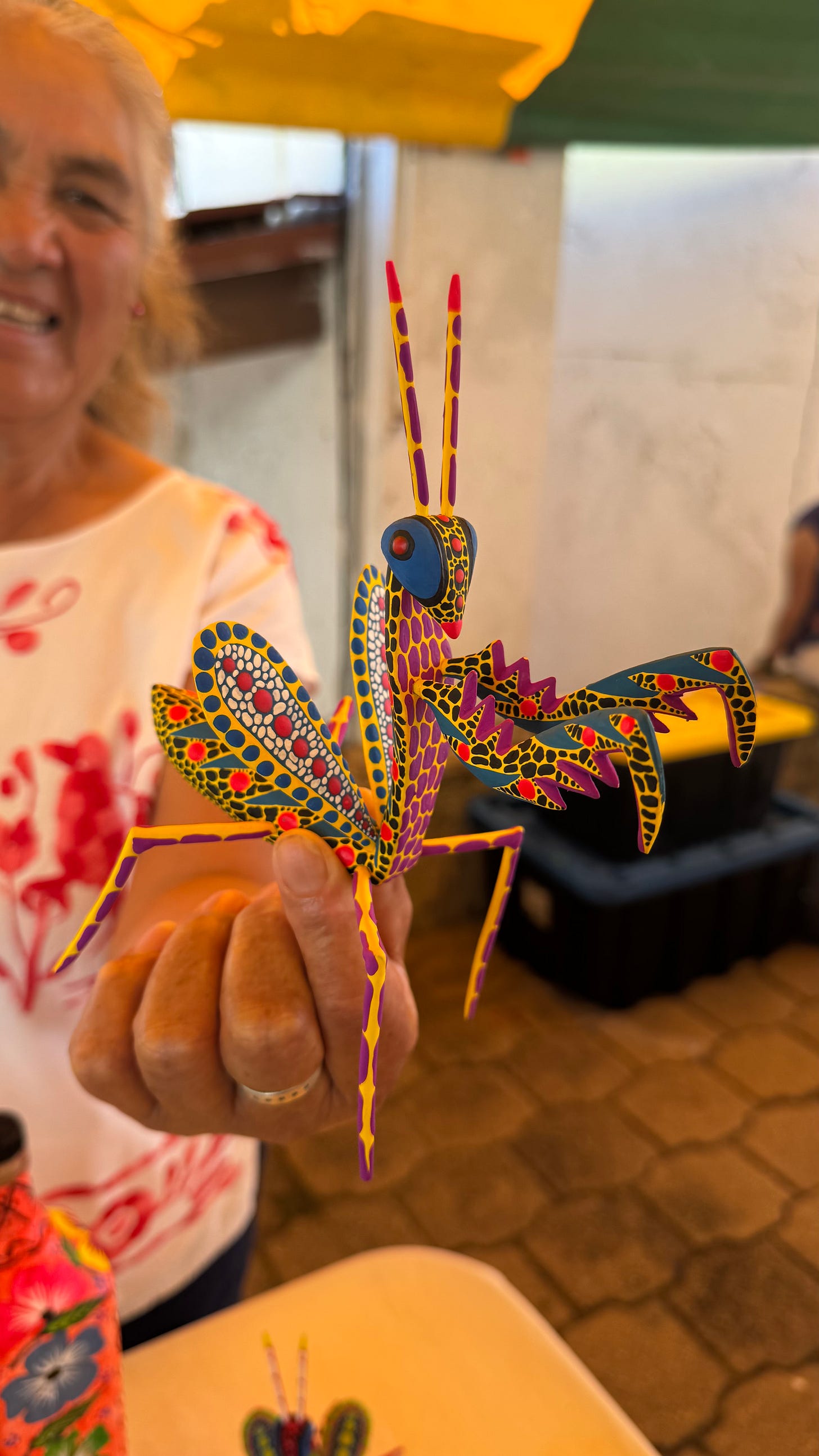 An alebrije of a praying mantis held in a woman's hand.