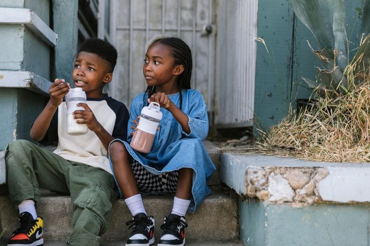 This may contain: two children sitting on the steps drinking from their coffee mugs and looking off into the distance